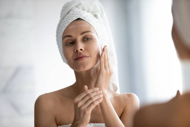 istock Head shot beautiful peaceful woman applying moisturizer on face 1209020105