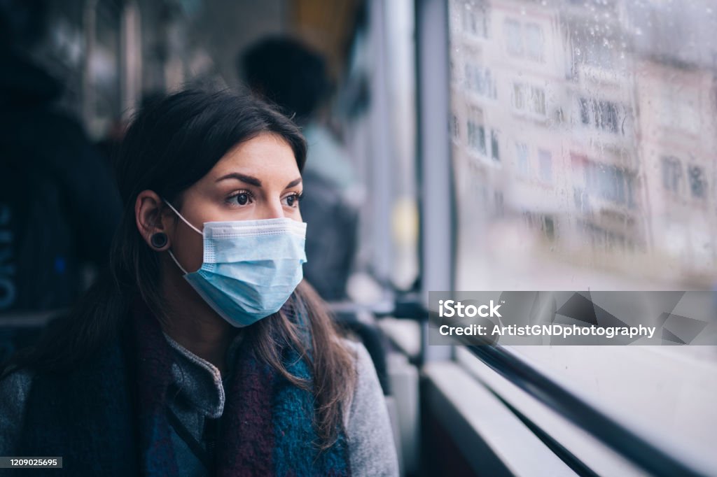 Worried Woman With Protective Face Mask In Bus Transport. Young woman wearing protective face mask, she sitting in bus transportation in the city. Protective Face Mask Stock Photo