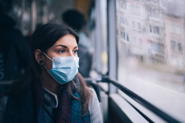 Worried Woman With Protective Face Mask In Bus Transport. Young woman wearing protective face mask, she sitting in bus transportation in the city. avian flu virus photos stock pictures, royalty-free photos & images