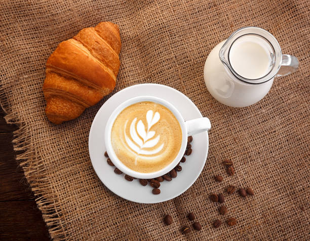 white cup of coffee on burlap carafe of milk grain