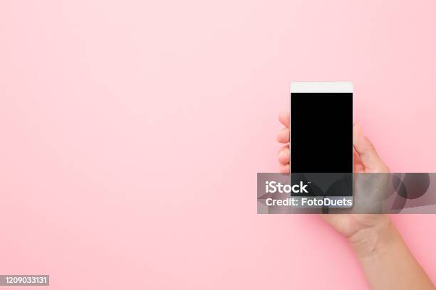 Young Woman Hand Holding Smartphone With Black Screen On Light Pink Table Background Pastel Color Empty Place For Text Closeup Top Down View Stock Photo - Download Image Now