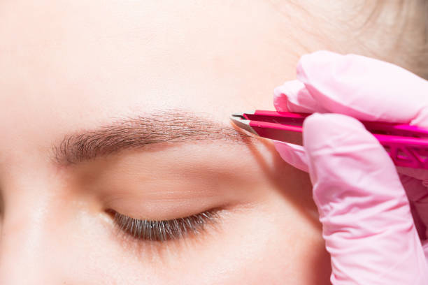 istock Eyebrow shape correction procedure with tweezers. Young female face close-up. 1209040043
