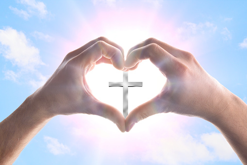 Hands of a man forming a heart in heaven with spikes surrounding a cross. Horizontal composition