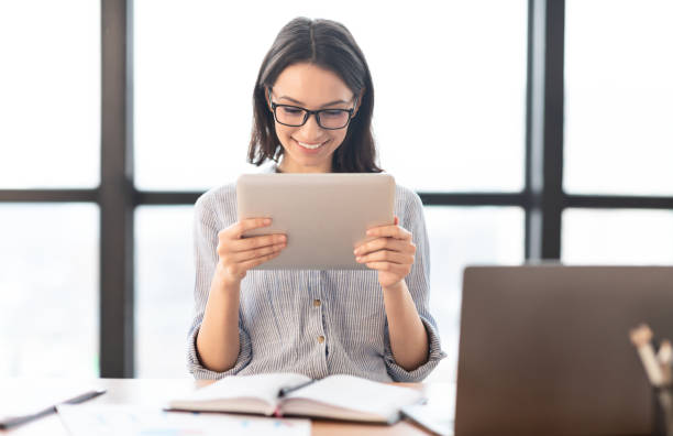 junges mädchen hält tablet und mit laptop in modernen büro - glasses touchpad professional occupation women stock-fotos und bilder