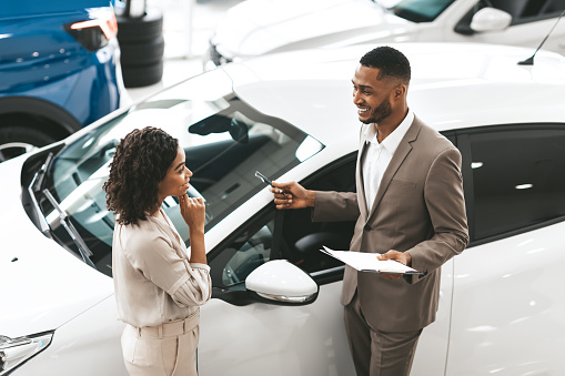 Gerente de ventas de automóviles que muestra auto a la señora de pie en el concesionario photo