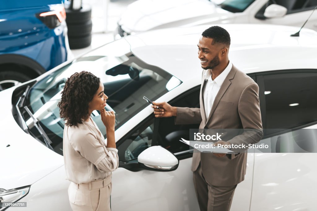 대리점에 서있는 레이디에게 자동차를 보여주는 자동차 판매 관리자 - 로열티 프리 자동차 대리점 스톡 사진