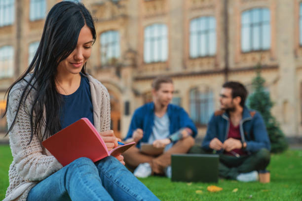 istock Young female student noting while two males using laptop in background at lawn 1209047779