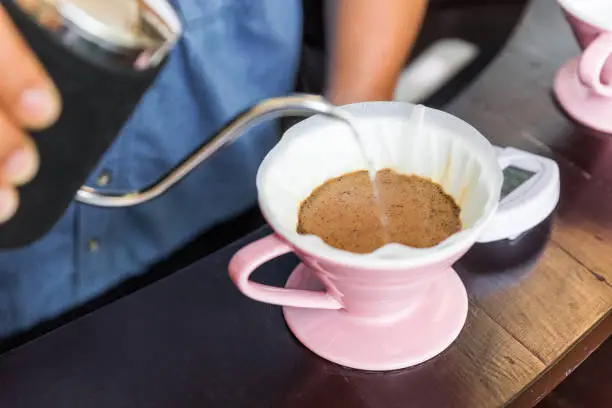 Close-up of Barista's hand, making pour-over coffee with alternative method called Dripping. Pink Coffee grinder, coffee stand and pour-over on a wooden counter.