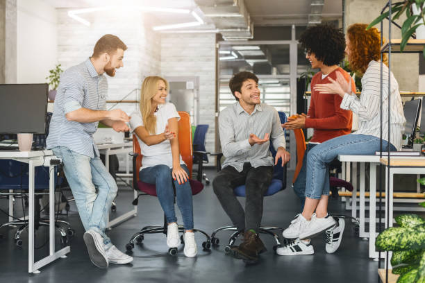 Cheerful millennial team having pleasant conversation in office Informal business meeting. Cheerful millennial creative team having pleasant conversation in office office buddies stock pictures, royalty-free photos & images