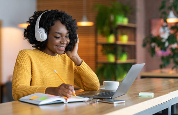 坐在耳機裡的黑人女孩在網上學習，在咖啡館使用筆記本電腦 - 吧 公共飲食地方 圖片 個照片及圖片檔