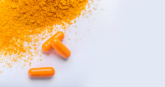 Supplement pills of curcumin or turmeric with a heap of the spice in dry powder, gray background, copy space, panorama