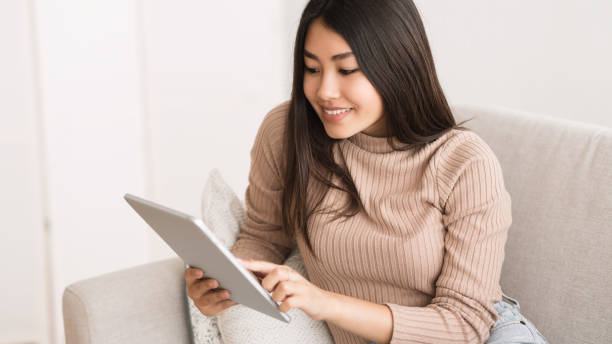 happy asian girl watching media content on tablet - kindle book reading digital display imagens e fotografias de stock