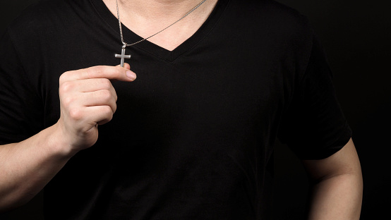Silver crucifix or cross pendant and necklace on body or hand studio shot black color background which represent to praying for god or jesus for christian religion people who have faith