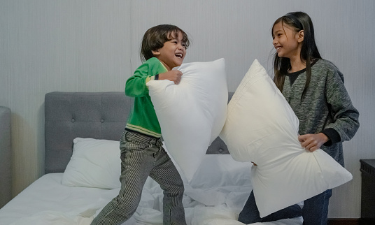 Photo of two kids playing with the pillows at their parents bedroom.