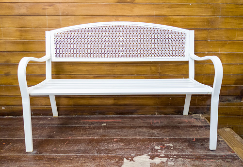 White metal bench in the retro style near the wooden terrace of the local bistro.