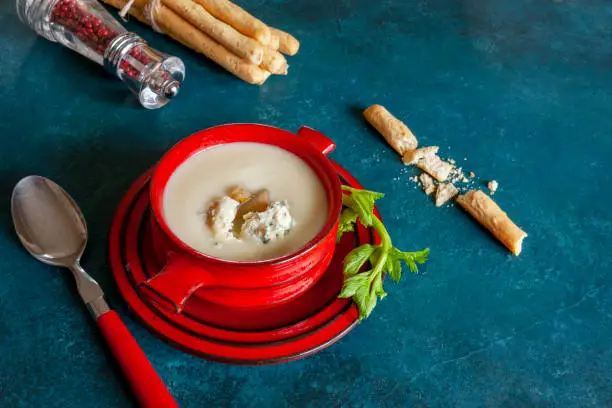 Vegetarian celery root homemade cream-soup with blue cheese, fresh caramelized pear and breadsticks. Close up, top view on the blue background