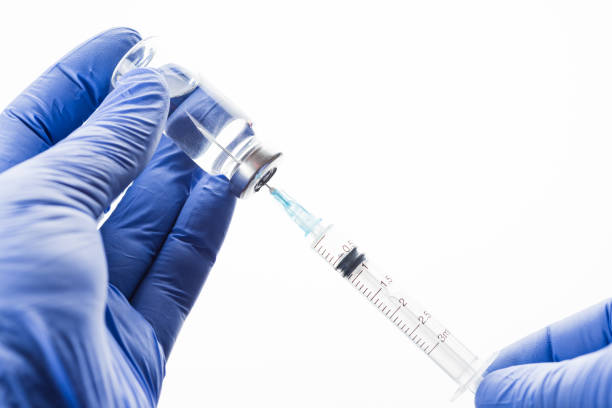 의사는 주사기를 채웁니다. 파란색 라텍스 장갑을 낀 손에 투명한 항생제 또는 백신이있는 유리 병. - russian shot 뉴스 사진 이미지