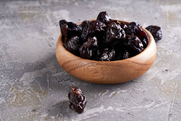 istock prunes, dried plums in a wooden bowl on a gray background Rustic style 1209073827