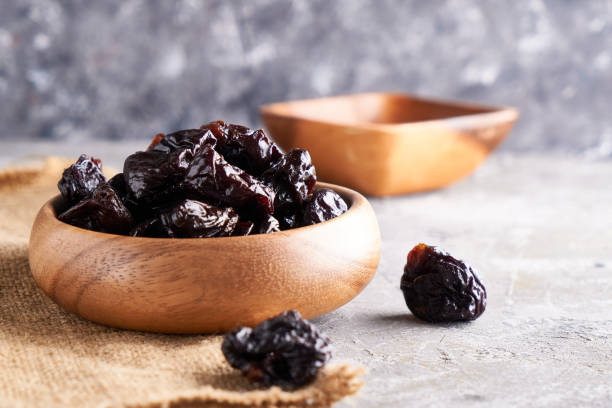 istock prunes, dried plums in a wooden bowl on a gray background Rustic style 1209073829