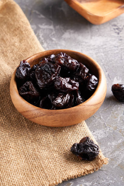 istock prunes, dried plums in a wooden bowl on a gray background Rustic style 1209073953