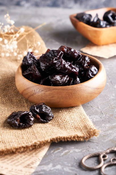 istock prunes, dried plums in a wooden bowl on a gray background Rustic style 1209074354
