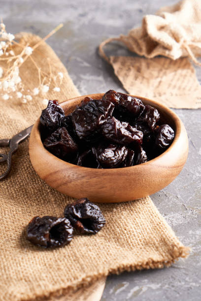 istock prunes, dried plums in a wooden bowl on a gray background Rustic style 1209074357