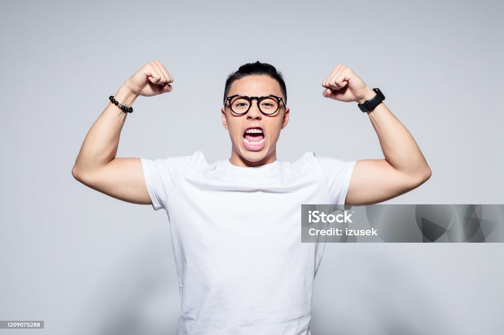 Excited asian winner Portrait of happy asian young man wearing white t-shirt and glasses, in winner gesture. Studio shot, white background. Shouting Stock Photo
