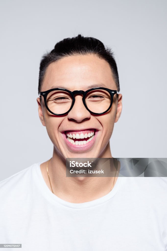 Excited asian young man laughing at camera Headshot of happy asian young man wearing white t-shirt and glasses, laughing at camera. Studio shot, white background. Hipster Culture Stock Photo