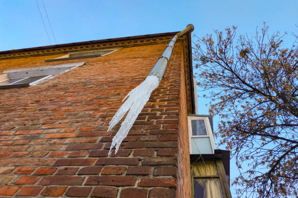 Icicles hang from the water pipe of a residential building. Thaw and warming winter weather. Ice blockage in the drainpipe.