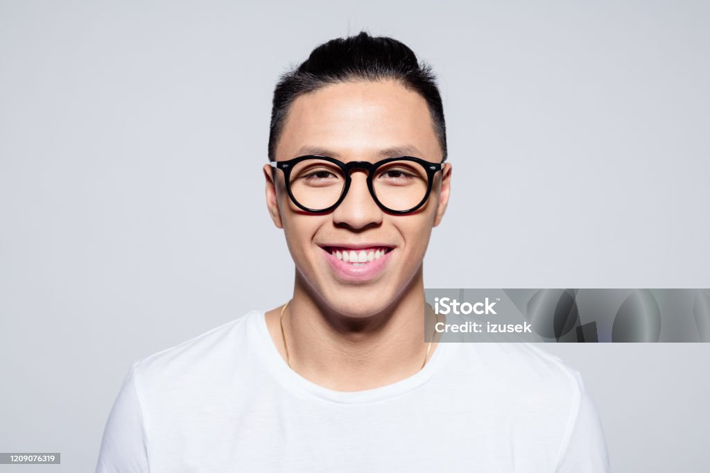 Friendly asian young man smiling at camera Headshot of happy asian young man wearing white t-shirt and glasses, smiling at camera. Studio shot, white background. 20-24 Years Stock Photo