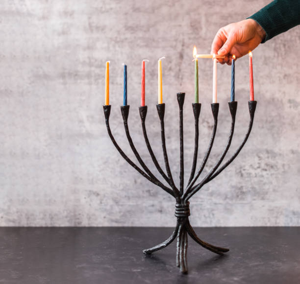 immagine ritagliata di una candela che accende a mano su menorah per hanukkah. - hanukkah menorah human hand lighting equipment foto e immagini stock