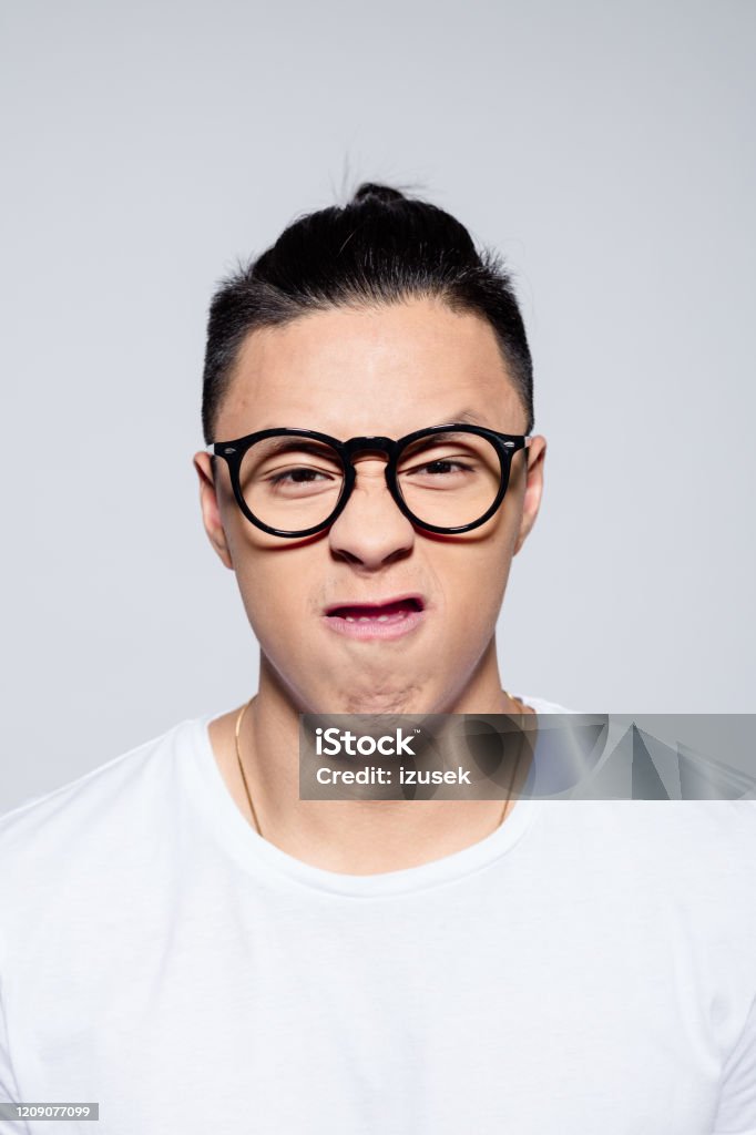 Portrait of angry asian young man Headshot of frustrated asian young man wearing white t-shirt and glasses. Studio portrait on white background. 20-24 Years Stock Photo