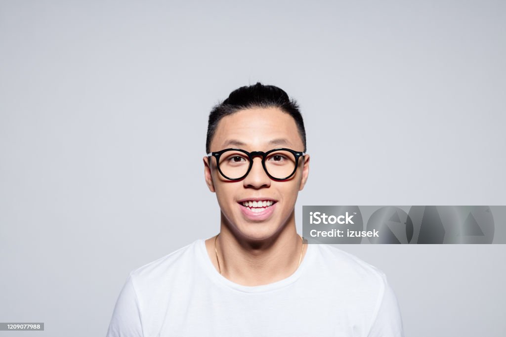 Portrait of friendly asian young man smiling at camera Headshot of happy asian young man wearing white t-shirt and glasses, smiling at camera. Studio portrait on white background. 20-24 Years Stock Photo