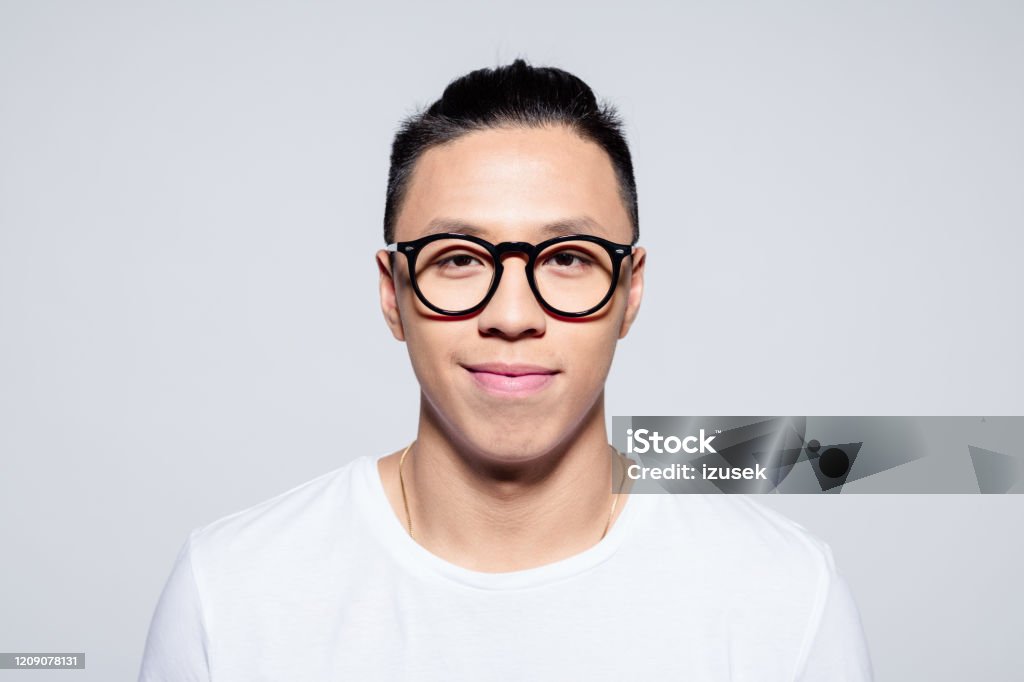 Portrait of friendly asian young man smiling at camera Headshot of happy asian young man wearing white t-shirt and glasses, smiling at camera. Studio portrait on white background. Headshot Stock Photo