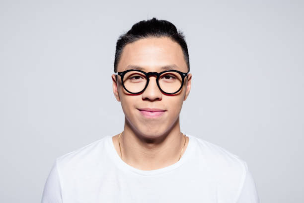Portrait of friendly asian young man smiling at camera Headshot of happy asian young man wearing white t-shirt and glasses, smiling at camera. Studio portrait on white background. smirking stock pictures, royalty-free photos & images