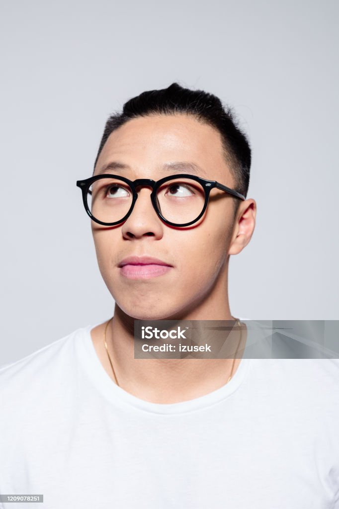Portrait of pensive asian young man Headshot of friendly asian young man wearing white t-shirt and glasses, looking away. Studio portrait on white background. White Background Stock Photo