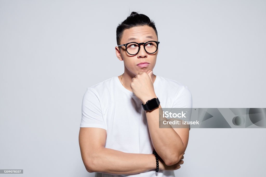 Portrait of pensive asian young man Headshot of asian young man wearing white t-shirt and glasses, looking away with hand on chin. Studio portrait on white background. Men Stock Photo