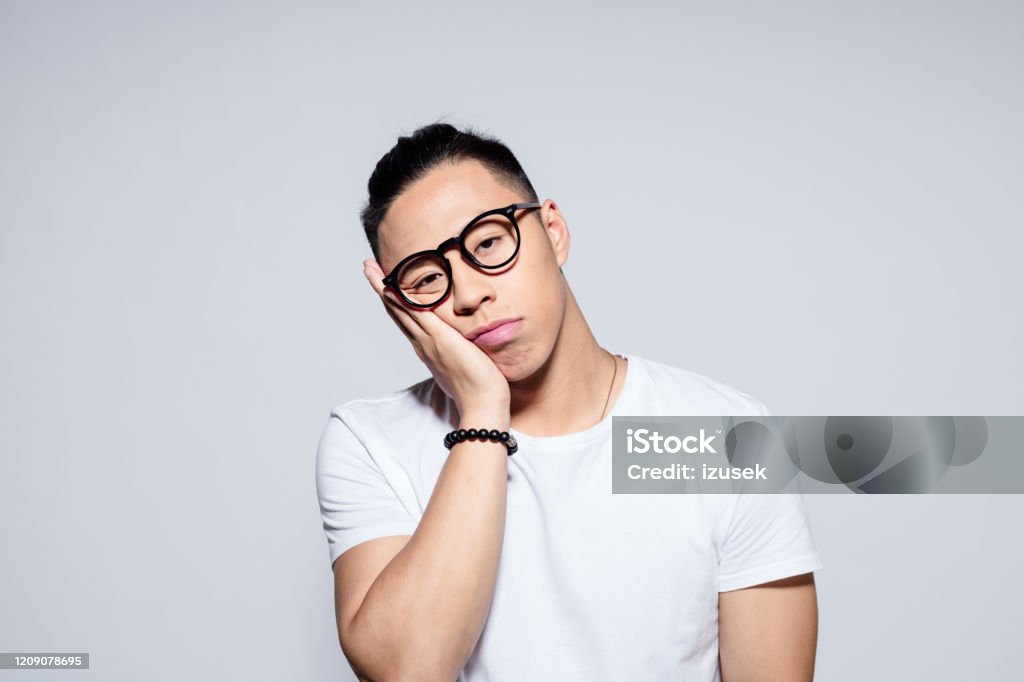 Worried asian young man Portrait of tired asian young man wearing white t-shirt and glasses, laughing at camera. Studio shot, white background. Men Stock Photo