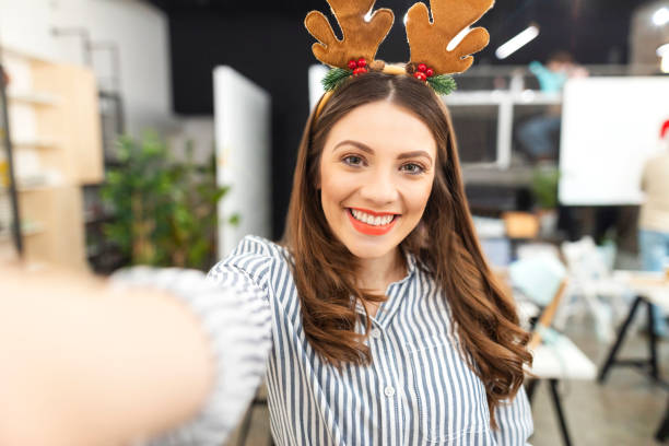 A New Perspective Young woman celebrating Christmas at her office and taking a selfie. office christmas party stock pictures, royalty-free photos & images