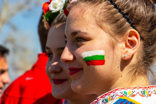 Varvara, Bulgaria - March 24, 2019: The Bulgarian flag painted on the face of a beautiful smiling Bulgarian girl in national costume