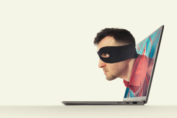 Concept of hacking and Identity theft. The human in a black mask moves through screen of a laptop.  Concept of hacking and Identity theft. synthetic identity theft stock pictures, royalty-free photos & images