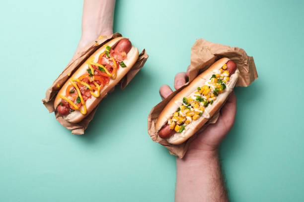 cropped view of man and woman holding two tasty hot dogs in paper on blue cropped view of man and woman holding two tasty hot dogs in paper on blue hot dog photos stock pictures, royalty-free photos & images