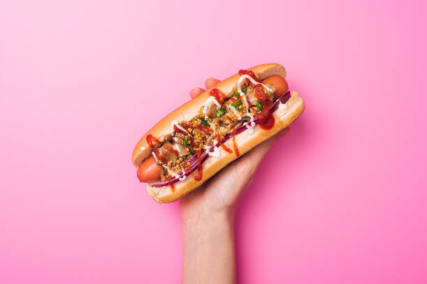 vue partielle de femme retenant le hot dog délicieux dans la main sur le rose - hot dog photos et images de collection