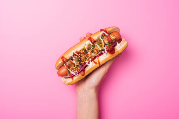 partial view of woman holding yummy hot dog in hand on pink partial view of woman holding yummy hot dog in hand on pink hot dog photos stock pictures, royalty-free photos & images