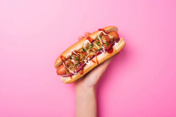 partial view of woman holding yummy hot dog in hand on pink