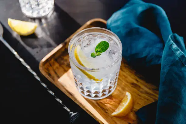 Photo of Refreshing cold summer cocktail with soda water, lemon and ice cubes on a wooden tray.