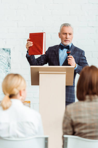 istock selective focus of auctioneer talking with microphone and holding book during auction 1209088833