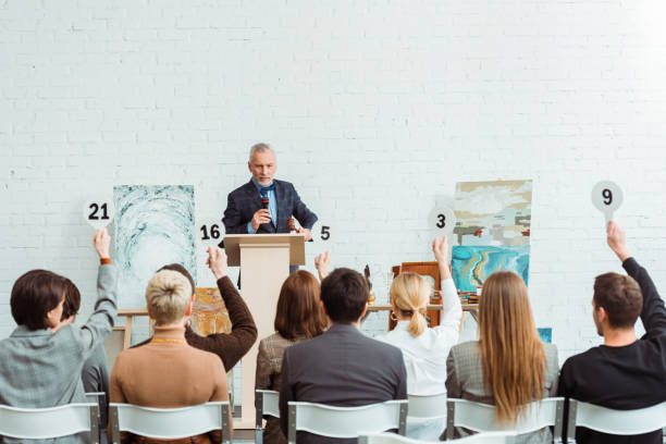 commissaire-priseur parlant avec le microphone et regardant des acheteurs avec des pagaies d’enchères pendant l’enchère - auction photos et images de collection