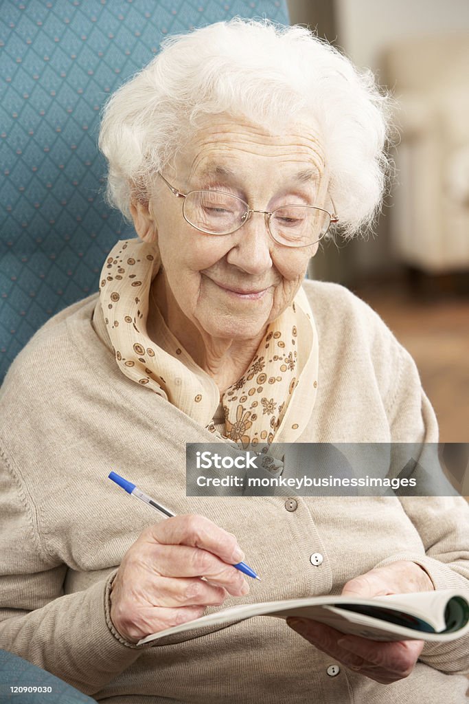 Mujer Senior relajante en casa de finalizar Crossword - Foto de stock de Mujeres mayores libre de derechos