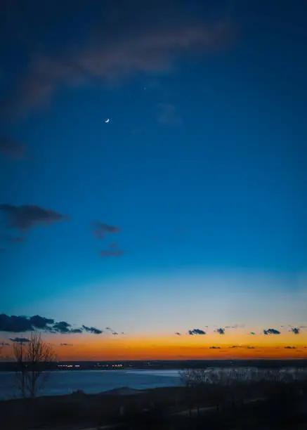 Photo of New moon over Pegwell Bay just after sunset when the sky is a Depp blue with an intense orange and red glow along the horizon